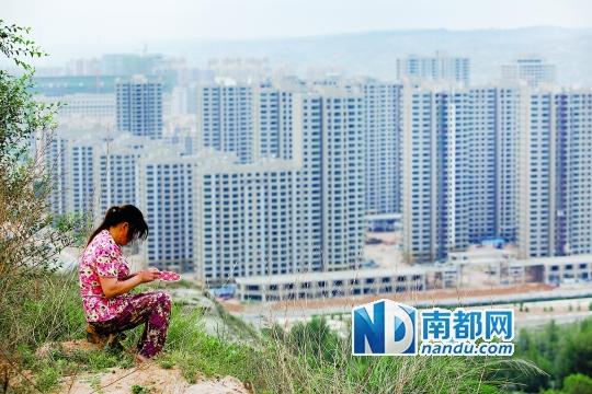神木新村西面的山坡上,一名磚窯的員工坐在坡頂繡鞋墊。席卷神木的民間借貸危機壓垮了當(dāng)?shù)貥鞘幸惨l(fā)債務(wù)危機,高樓林立的神木新村今年大部分工程已經(jīng)停工。南都記者孫俊彬攝